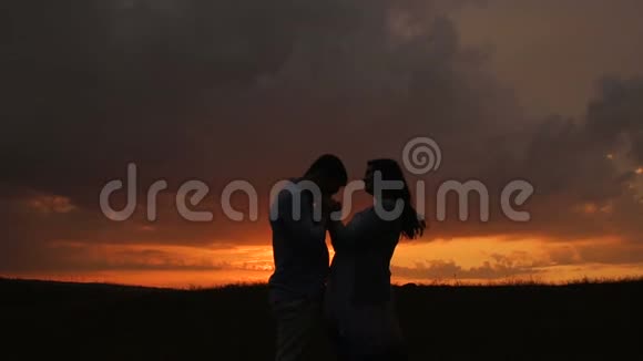 日落时分一位孕妇和她的丈夫在田野里的剪影慢动作视频的预览图