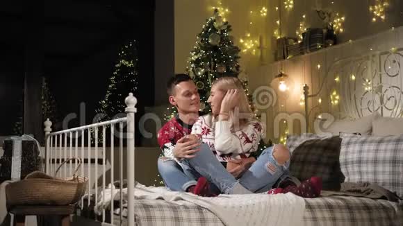 可爱的夫妇坐在床上背景是一棵装饰好的圣诞树视频的预览图