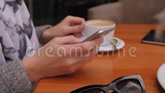 街边咖啡馆里一个拿着电话和一杯咖啡的女人的手特写镜头视频的预览图