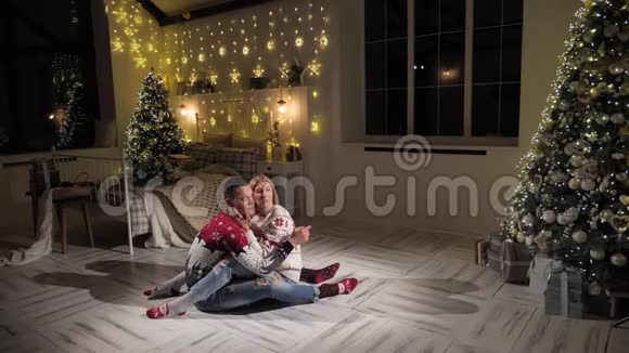 年轻幸福的一对夫妇正坐在圣诞树附近卧室的地板上视频的预览图