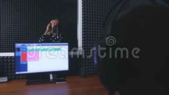 女歌手在麦克风中唱歌声音工程师在演播室录制歌曲视频的预览图