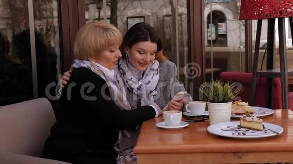 老年妇女和她的成年女儿使用智能手机在咖啡馆喝咖啡视频的预览图
