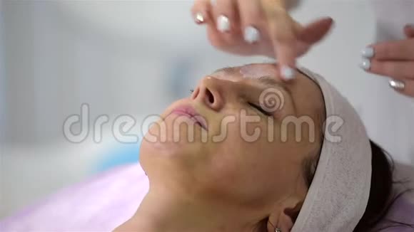 女孩美容师在客户脸上涂一种麻醉霜准备手术视频的预览图