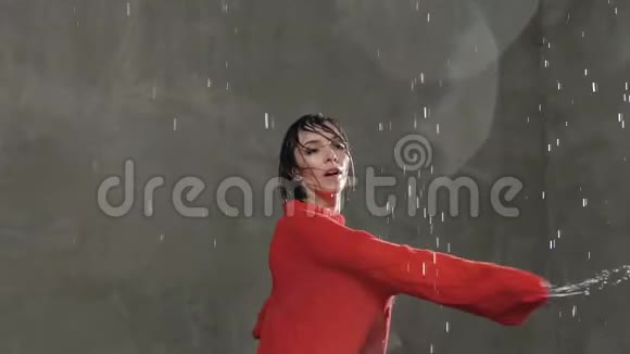 那位穿着红色毛衣的金发女郎在一片灰色背景下在雨滴的背景下在工作室里跳舞视频的预览图