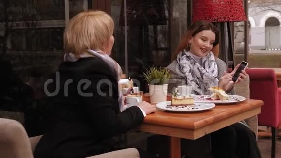 老年妇女和她的成年女儿用电话在人行道咖啡馆喝咖啡视频的预览图