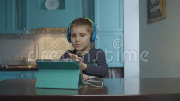 自闭症男孩在厨房里用带耳机的平板电脑有自闭症的孩子在家里四处张望自闭症视频的预览图