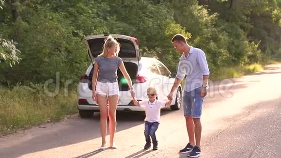一个小男孩和他的父母在靠近汽车的道路上跳跃后备箱打开视频的预览图