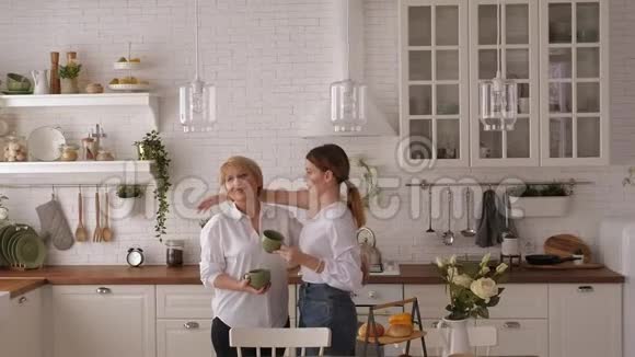 年轻女子和年迈的母亲在家中的现代厨房喝茶视频的预览图