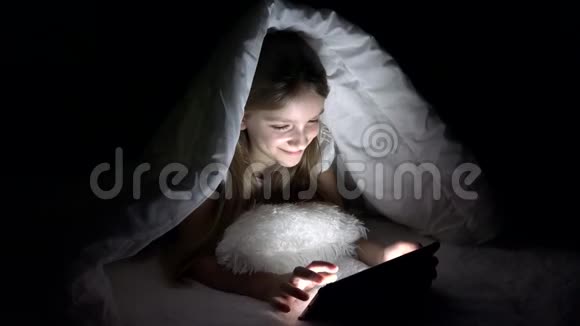 孩子在黑暗的夜晚玩平板电脑女孩在床上浏览互联网而不是睡觉视频的预览图