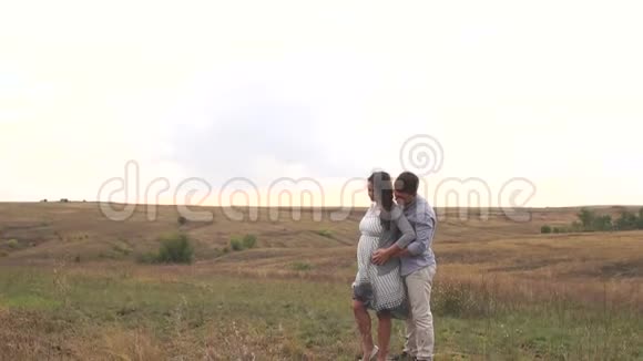 孕妇和她的丈夫一起抱着肚子在田野上视频的预览图