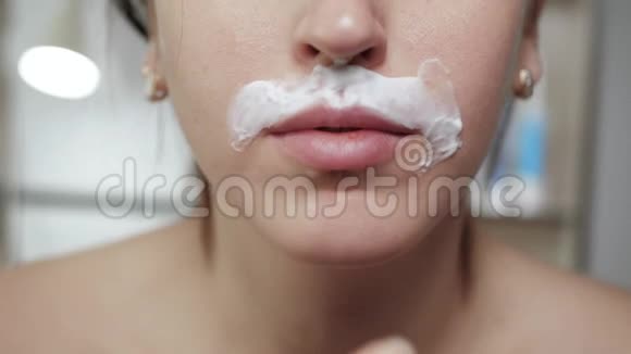 剃女性胡子的概念年轻迷人的白种人女孩用手指在脸上涂抹剃须泡沫关闭视频的预览图