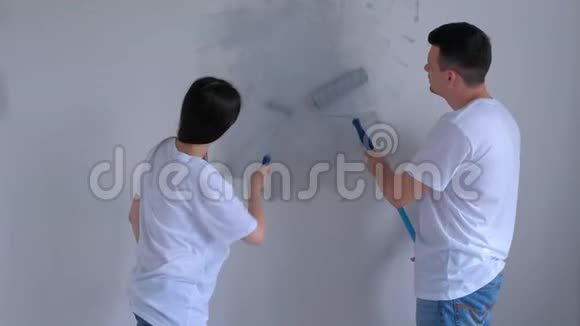 画家女孩和男孩正在用油漆滚筒和亲吻来粉刷灰色的墙壁视频的预览图