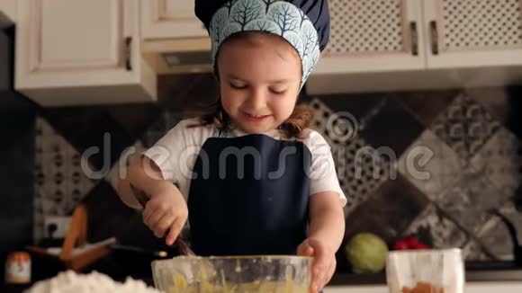 可爱的小微笑女孩穿着围裙和厨师帽正在揉面视频的预览图