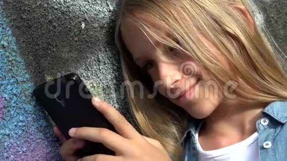 孩子使用智能手机孩子玩智能手机女孩在公园户外视频的预览图
