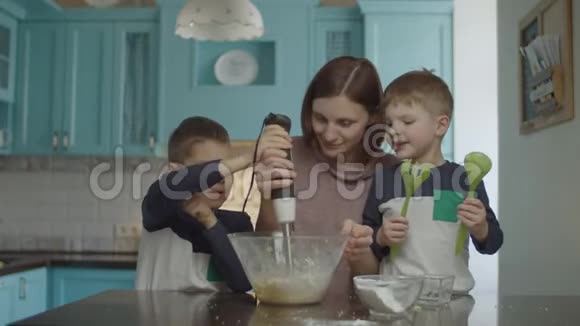 孩子们帮妈妈用搅拌器揉面团快乐的家庭烹饪饼干和享受蓝色家庭乐趣视频的预览图
