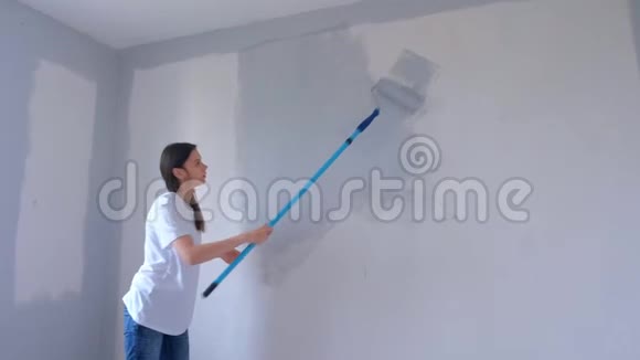 单身的年轻女子正在用新的平面上的油漆滚筒在灰色的墙壁上画画视频的预览图