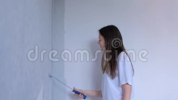 单身的年轻女孩画家是用平滚筒在灰色的墙壁上作画视频的预览图