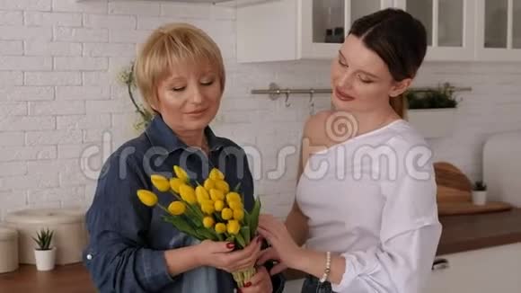 一位妇女在现代化的厨房里给她年迈的母亲一束郁金香视频的预览图