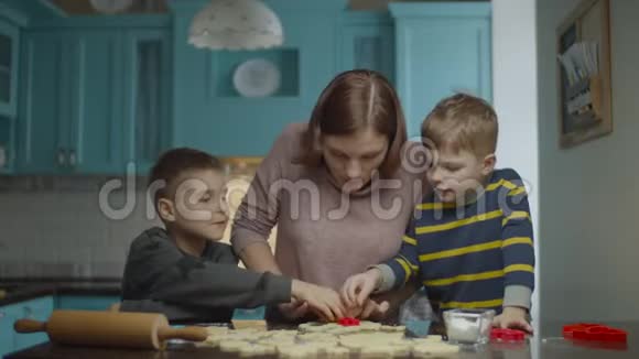 年轻的母亲和两个儿子烹饪不同形状的面团孩子们帮妈妈在家蓝厨房做糖果视频的预览图
