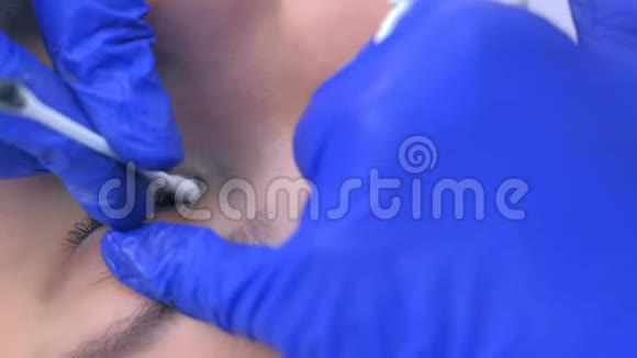 美容师从女性眼睑上擦拭油漆制作永久眼线视频的预览图