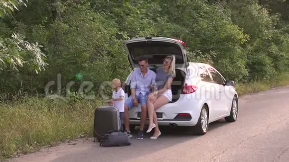 有儿子的父母坐在空路上的汽车后备箱里家人在度假视频的预览图