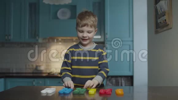 一个金发的学龄前男孩在家厨房里把塑料帽按颜色排成一排孩子做完后举起手来视频的预览图