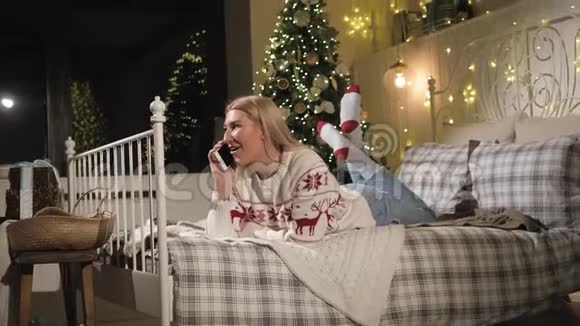 十几岁的女孩躺在圣诞树附近的床上正在打电话视频的预览图