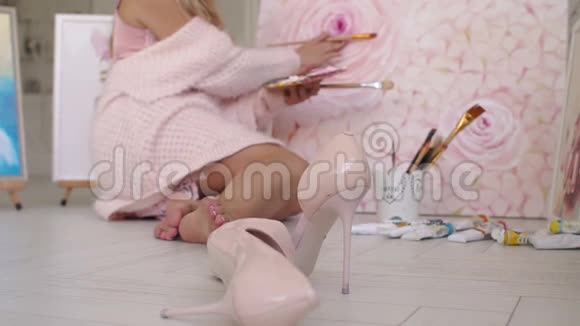 一个穿着粉红色睡衣和毛衣的年轻女孩坐在地板上的帆布上画画视频的预览图