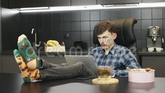 男人坐在厨房里在家里用笔记本电脑放松和在线工作年轻男性使用笔记本在家庭办公室工作视频的预览图