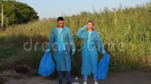 两个穿着蓝色长袍和手套的志愿者站在河岸上的垃圾中视频的预览图