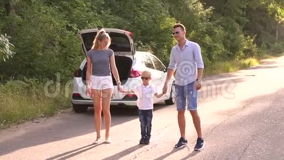 一家人带着一个孩子在一辆车旁边的肖像空路上有一条敞开的后备箱视频的预览图