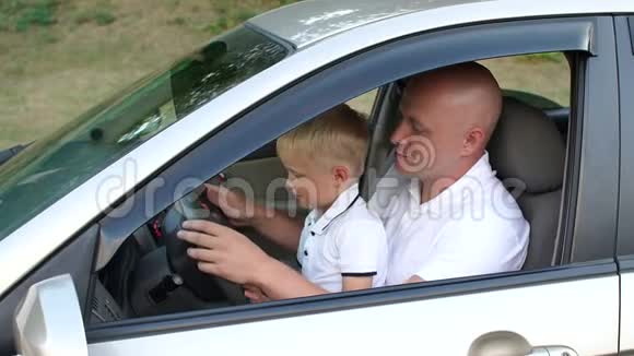 一个年轻的爸爸教他的小儿子开车他们坐在方向盘上视频的预览图