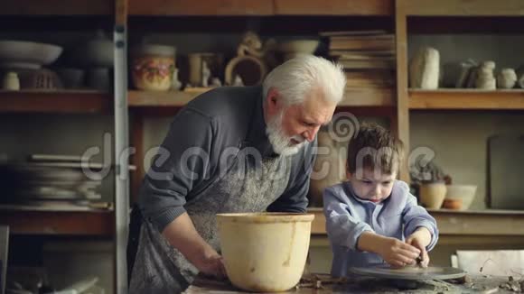 陶艺老师资深大人正在帮助年轻的学生用一块粘土在投掷轮上形成锅可爱的男孩视频的预览图