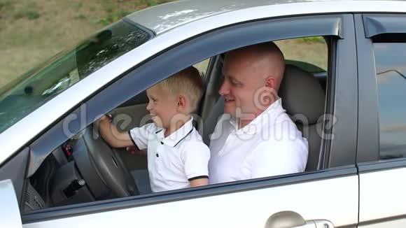 小男孩坐在他父亲开汽车的腿上他们学会开车视频的预览图