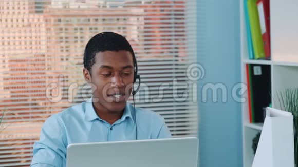 在耳机里和某人说话在电脑上工作的黑人特写视频的预览图