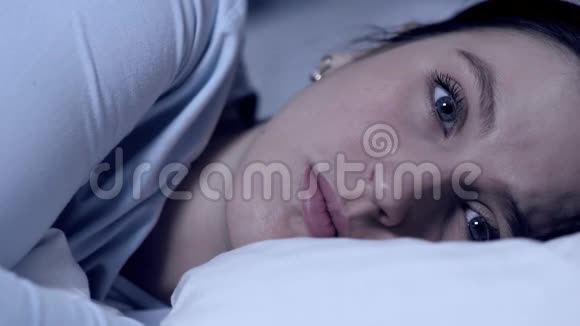 女孩不能睡着失眠的概念年轻迷人的白种人女孩独自躺在床上眨着眼睛看着视频的预览图
