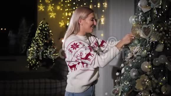 一个穿着针织毛衣的年轻快乐女孩正在家里装饰圣诞树视频的预览图