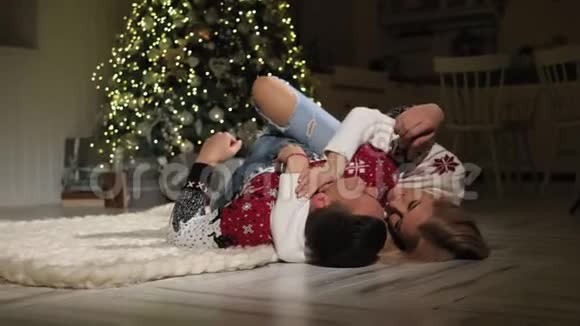 一对穿着圣诞毛衣的夫妇躺在地板上笑得很开心视频的预览图