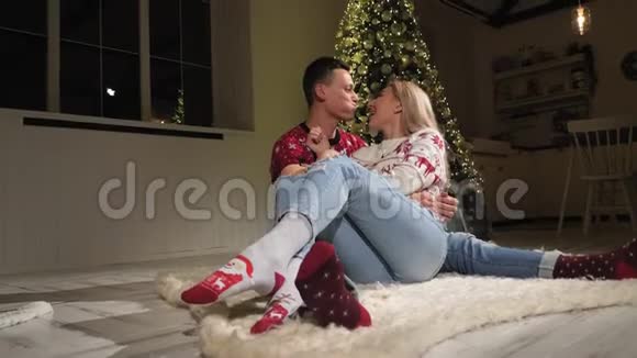 一对幸福的夫妇在家中的圣诞树附近的地板上玩得很开心他们亲吻视频的预览图