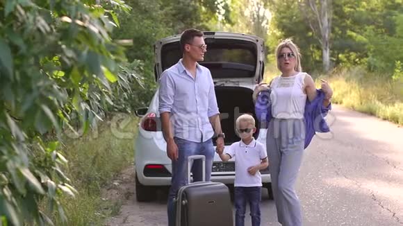 一个幸福的家庭的肖像一个手提箱靠近一条空路上的汽车后备箱视频的预览图