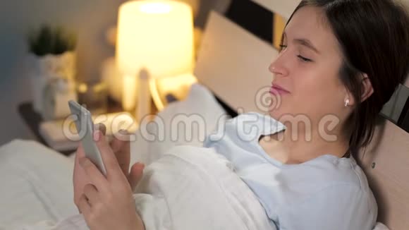 女孩睡觉前打电话冲浪年轻漂亮的女人躺在床上把手指放在手机屏幕上视频的预览图