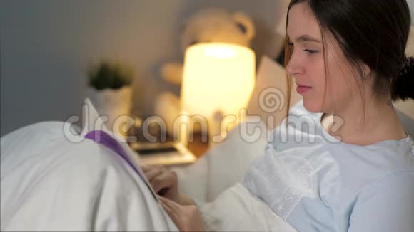 女孩在看书年轻迷人的白种人女人晚上躺在床上拿着毯子看书和喝酒视频的预览图