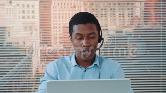 戴耳机的黑人男子与某人交谈并在电脑上工作视频的预览图