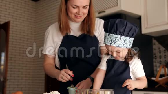 戴着帽子和围裙的小女孩在和妈妈一起做松饼时吃面团视频的预览图