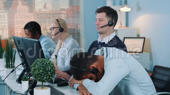 中镜头黑色客户支持接线员在呼叫中心的桌子上睡着了视频的预览图