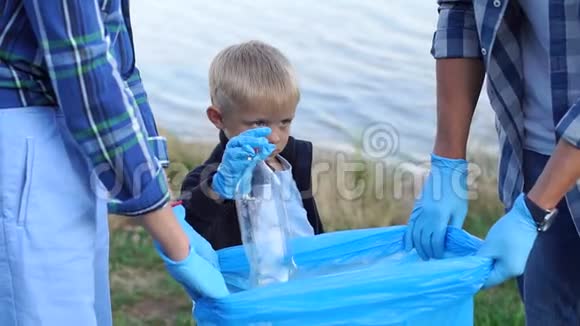 一个戴手套的小男孩帮助志愿者在公园里收集塑料垃圾视频的预览图