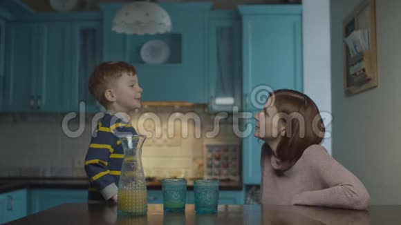 金发的学龄前儿童在厨房里和妈妈说话桌上放着苹果汁孩子给妈妈讲故事视频的预览图
