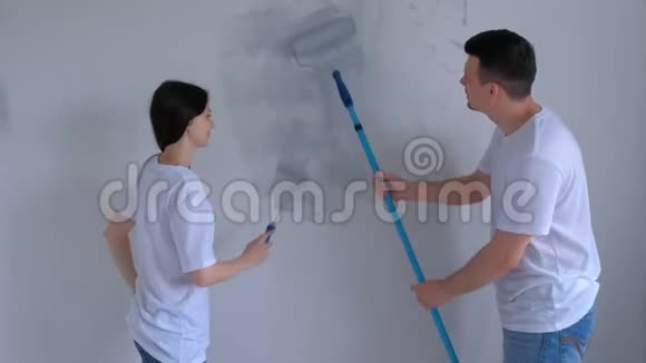 画家年轻的女孩和男孩正在用油漆滚筒在灰色的墙壁上画画视频的预览图