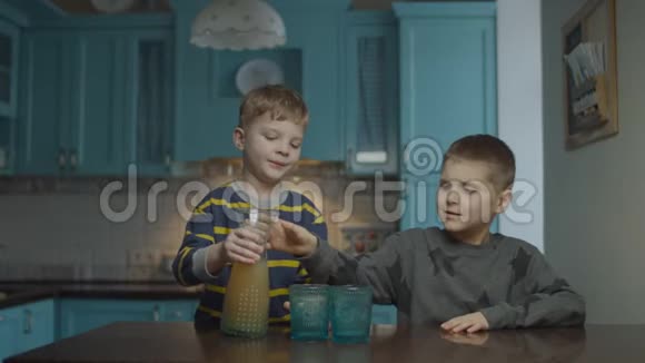 两个男孩在厨房里喝苹果汁弟弟把杯子里的果汁倒进去兄弟姐妹视频的预览图
