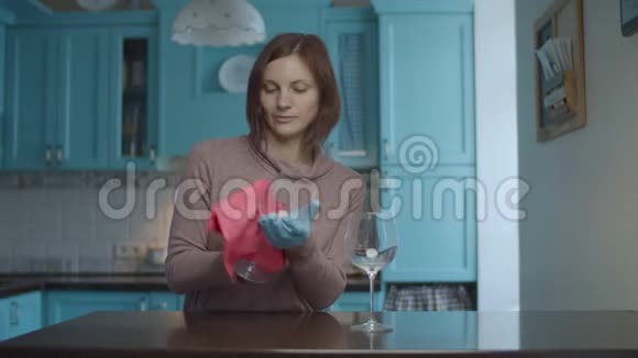 年轻的30多岁的女性戴着手套用粉红色的餐巾擦着眼镜在蓝色的厨房里跳舞女人很幸福视频的预览图